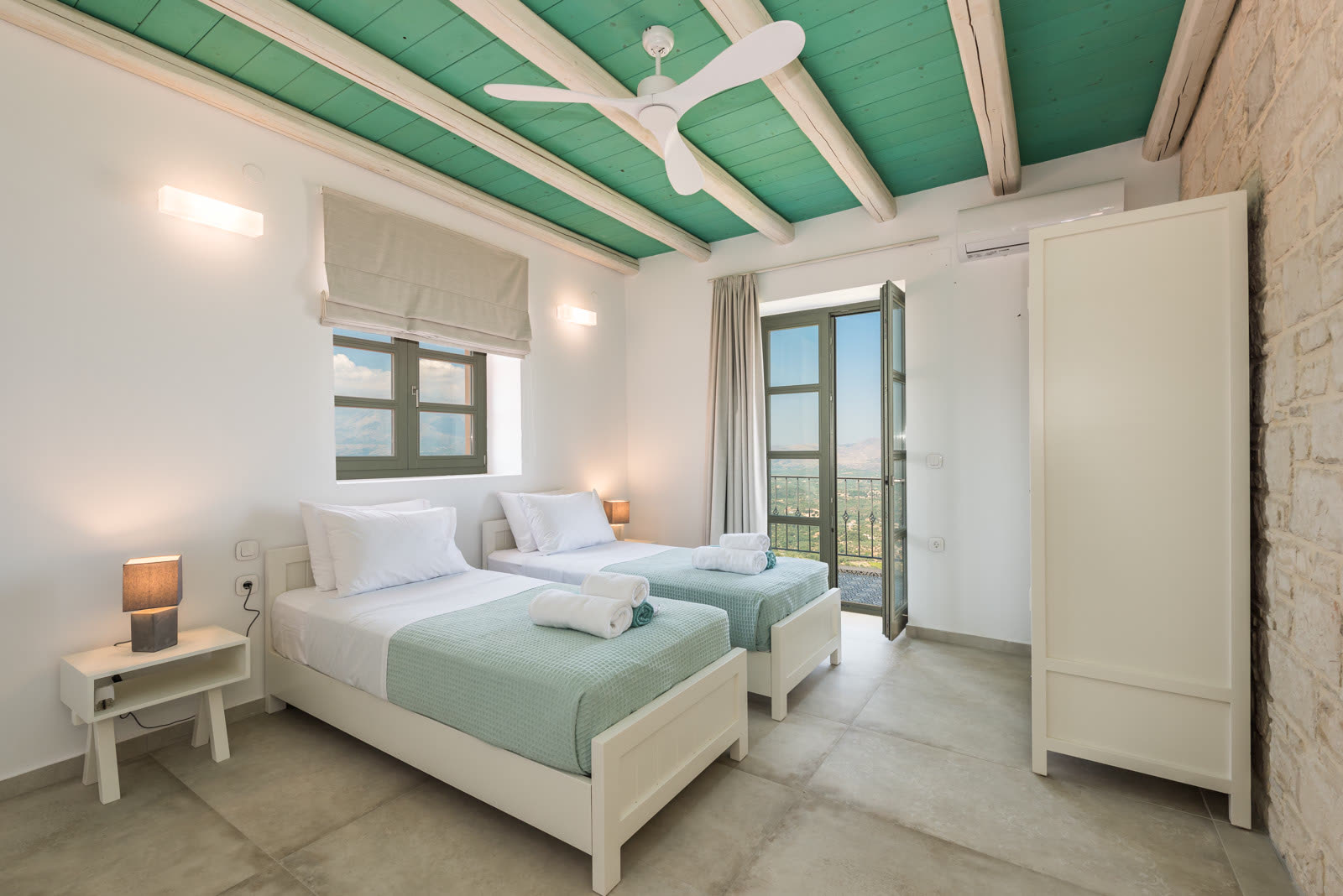 Twin bedroom with teal beamed ceiling, stone wall and balcony