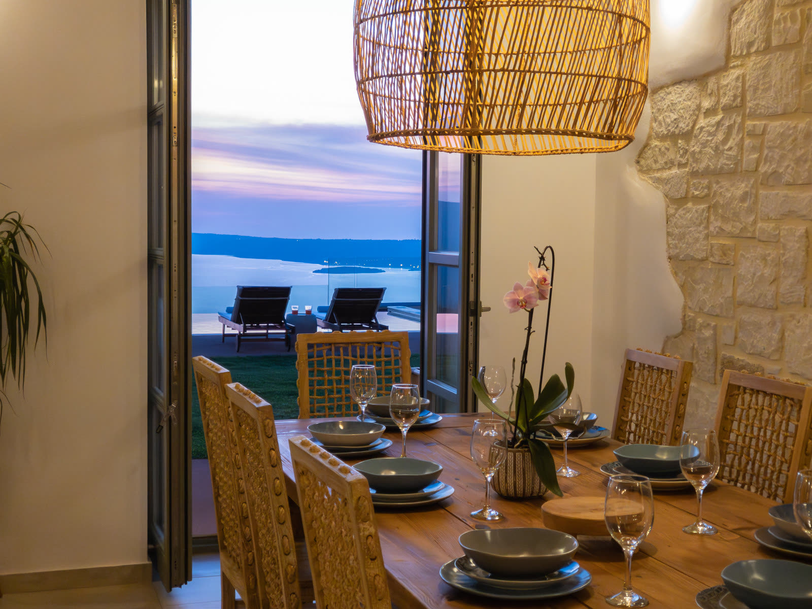 Indoor dining table looking through open doors to the pool and sea at dusk
