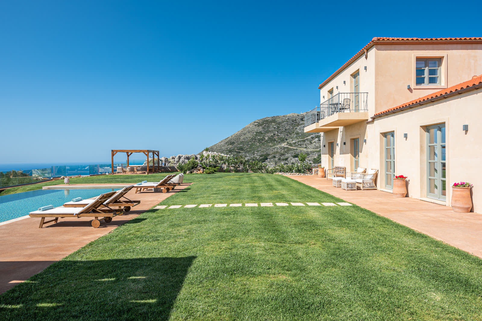 Manicured lawn, stepping stones, pool and villa with sea in the distance