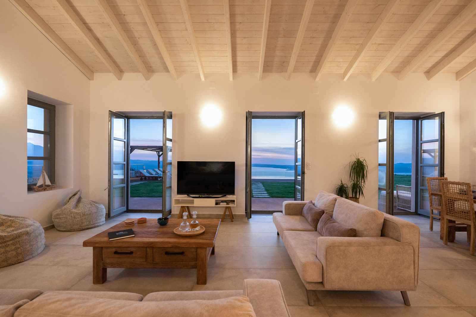 Living room with cream sofas, open terrace doors and a view to the lawn and sea