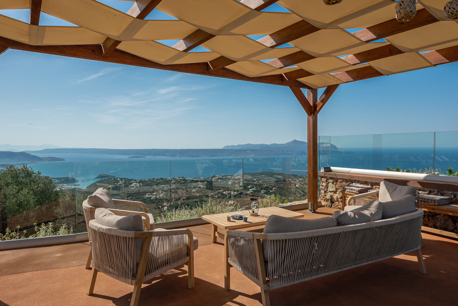 Shaded outdoor lounge under a wooden pergola overlooking the sea