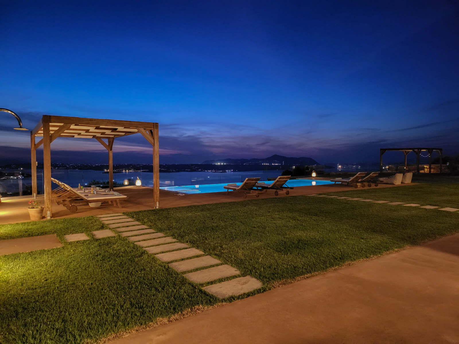 Infinity pool glowing at twilight with village lights on the coast