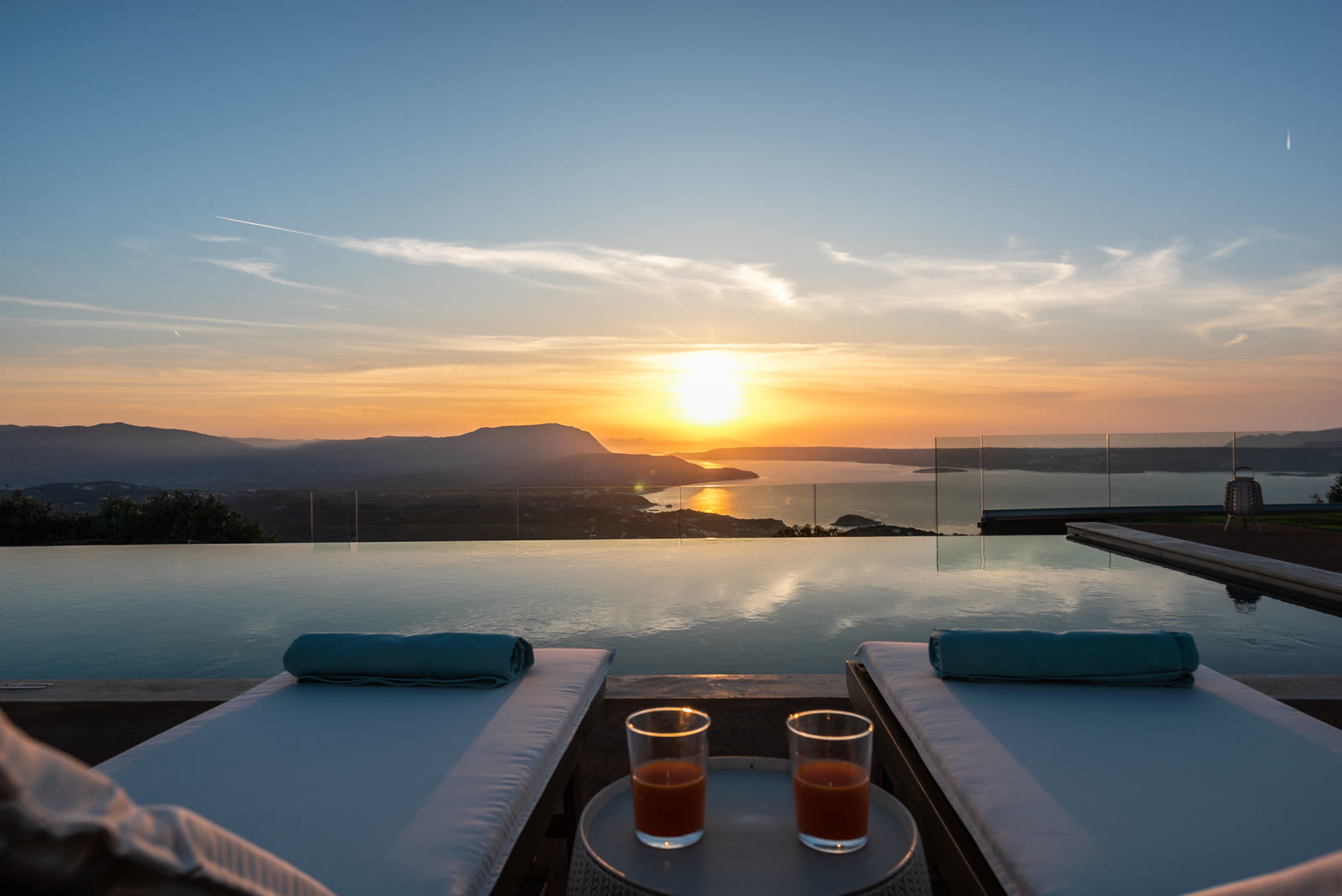Sunset over the Cretan north coast from the infinity pool at Aquila Villa, with sun loungers facing the horizon